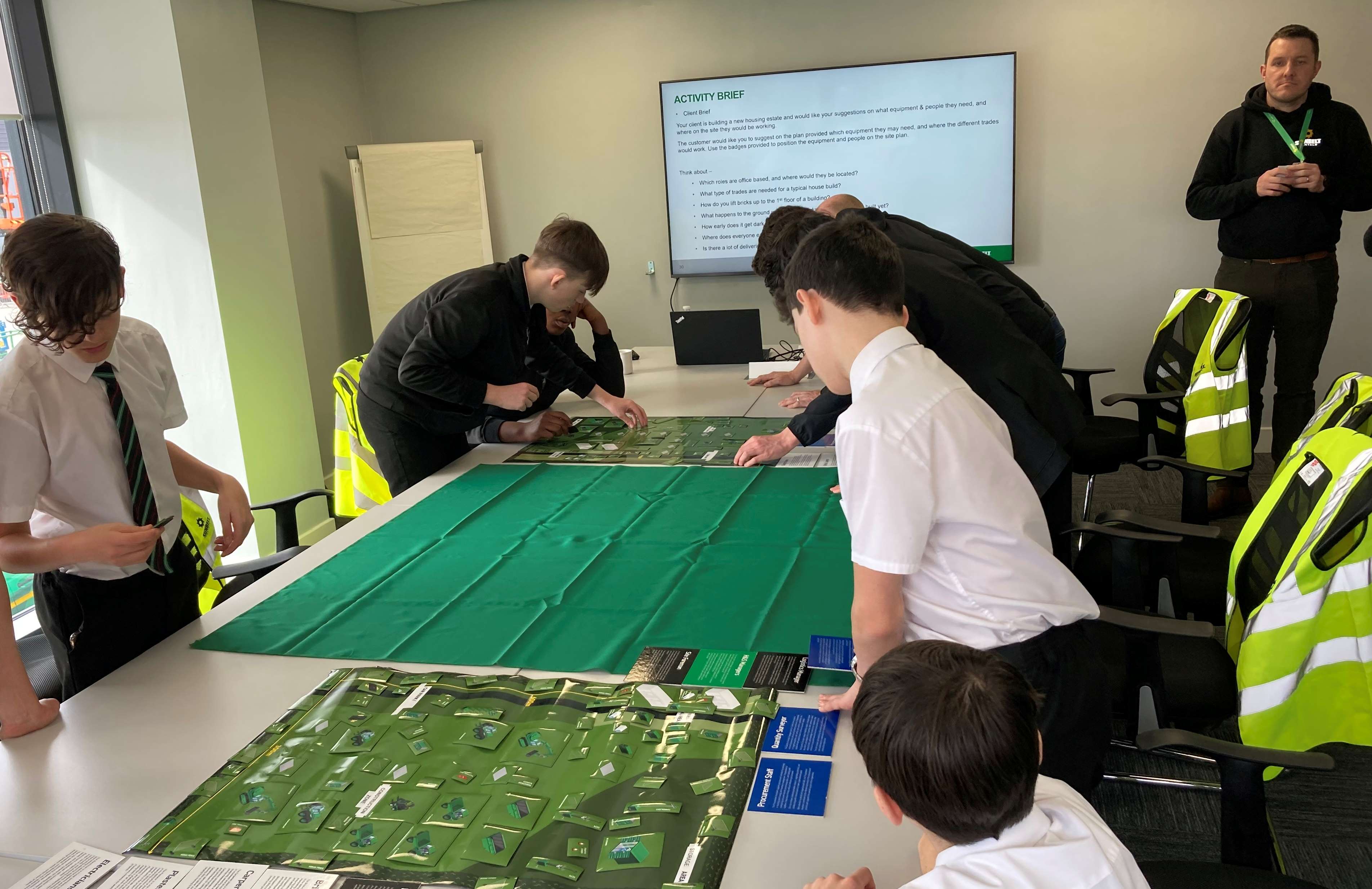 A group of school-age students in uniform lean over a large table, working on an interactive activity.